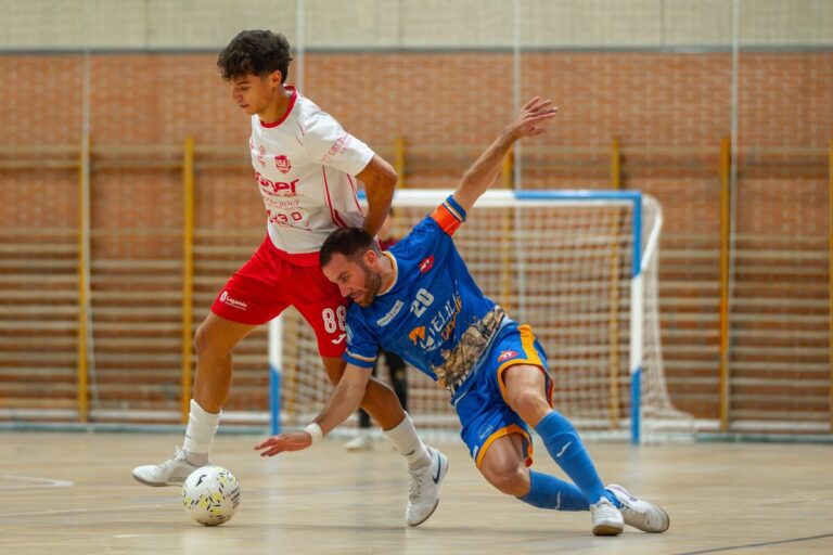 Two futsal players contest the ball during an indoor match, one in white/red and the other in blue as they clash near the goal area.