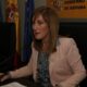 María Dolores Valverde sentada ante una mesa, con banderas y un rótulo institucional