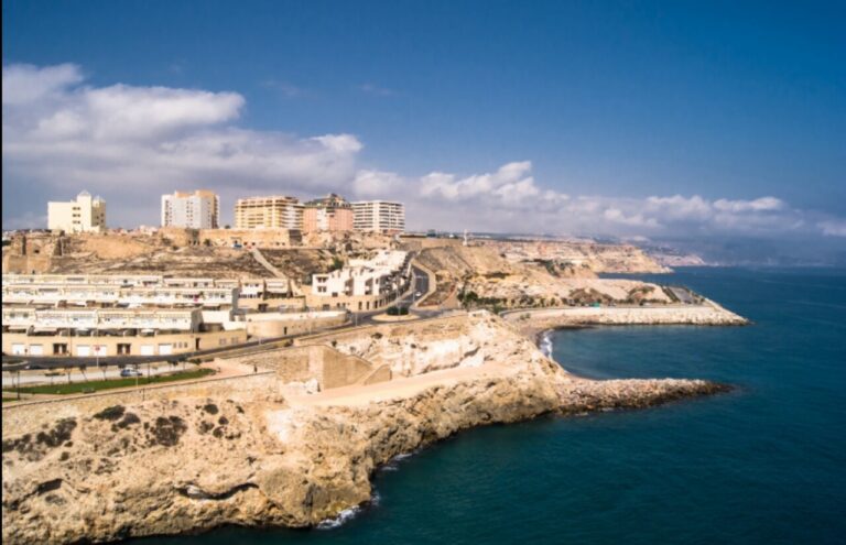 Vista costera de Melilla con edificios sobre acantilados y el mar azul.