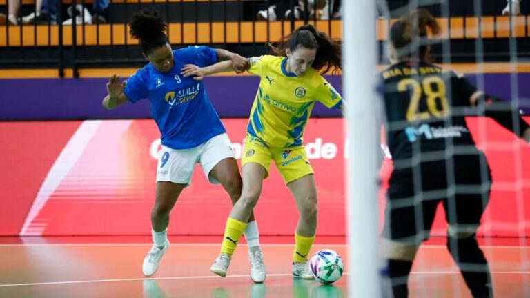 Dos jugadoras disputan el balón en una pista de fútbol sala, frente a la portera.