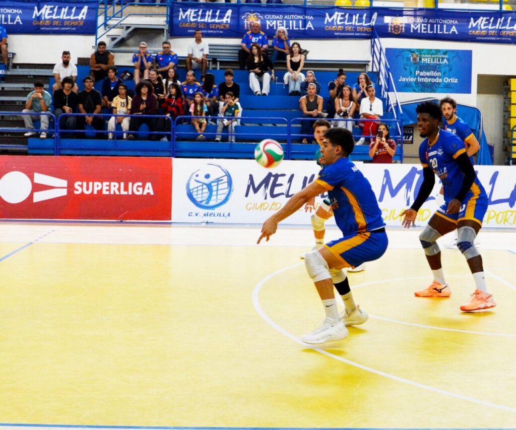 Jugadores de voleibol con uniforme azul y amarillo se preparan para recibir el balón.