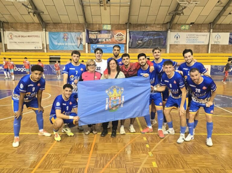 Grupo de jugadores con camisetas azules posa junto a una bandera en una pista cubierta.