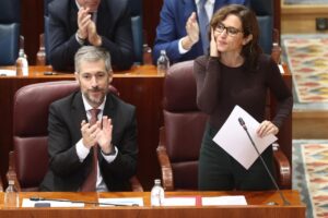 Una mujer sostiene documentos junto a un hombre que aplaude en una cámara parlamentaria.