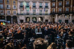 Una multitud rodea a un hombre que habla ante un micrófono frente al ayuntamiento.