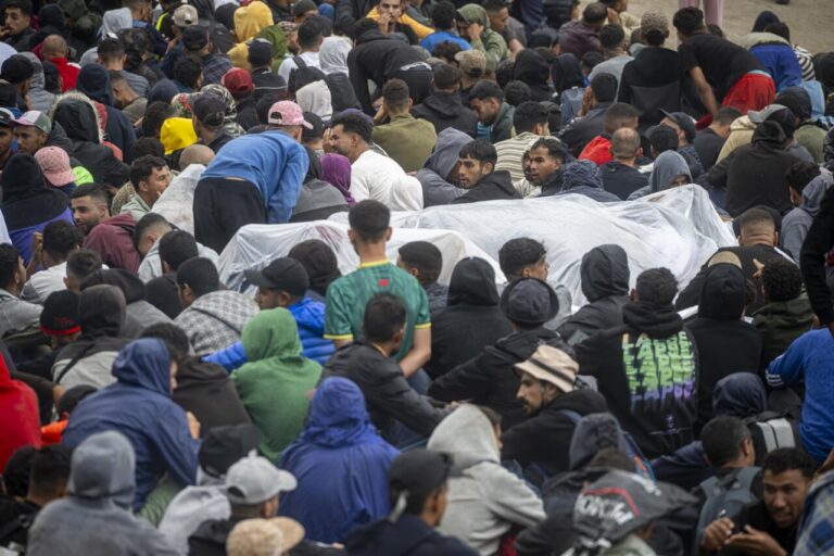 Multitud de personas apiñadas, muchas sentadas y algunas junto a grandes lonas blancas.