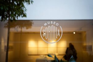 Rótulo del Museo Sorolla sobre un escaparate iluminado, con reflejos de árboles.