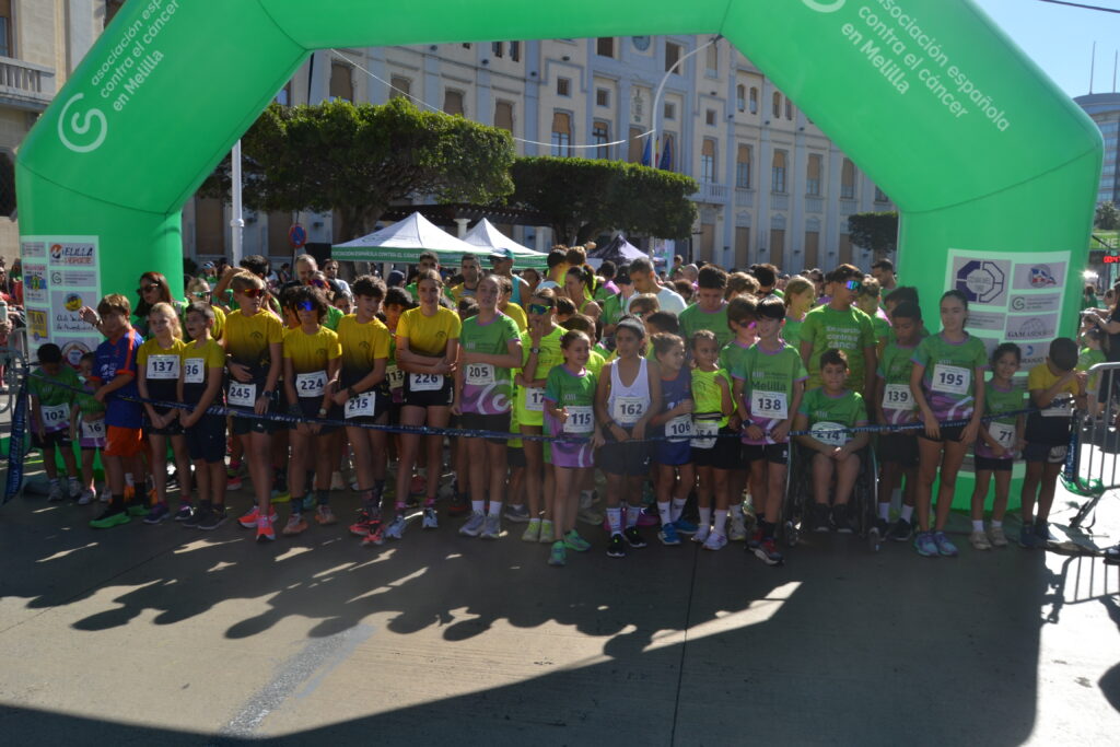 Participantes de distintas edades se agrupan bajo un arco verde de una carrera solidaria en Melilla.