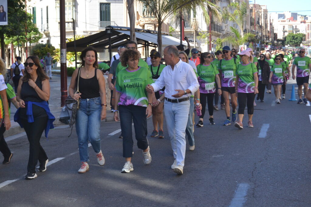 Participantes caminan por una calle con camisetas verdes de la marcha en Melilla.