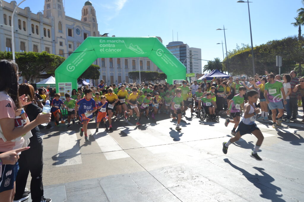 Participantes, muchos niños, corren bajo el arco verde de la marcha contra el cáncer.