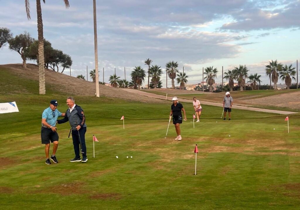 Varias personas juegan al golf en un campo con palmeras y banderines.