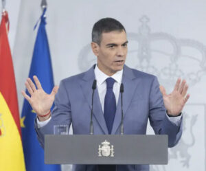 Pedro Sánchez habla ante un atril con micrófonos y banderas institucionales.