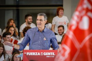 Politician speaks at a podium with a crowd behind, banner reads 'La Fuerza de la Gente' in red and white.