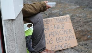 Persona sentada junto a un cartel manuscrito que solicita ayuda para comer