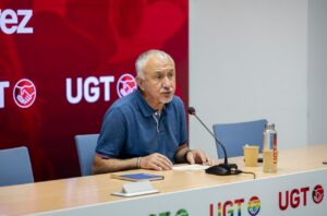 Hombre sentado ante un micrófono en una mesa con logotipos de UGT