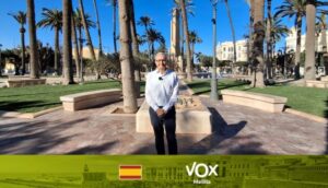 Persona de pie en una plaza arbolada, frente a un rótulo de VOX Melilla.