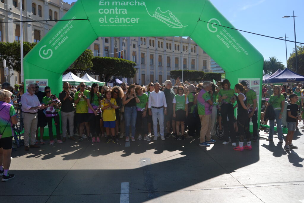 Personas reunidas bajo un arco verde de la marcha contra el cáncer en Melilla