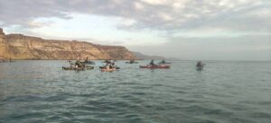Varias personas pescan desde kayaks frente a una costa rocosa.