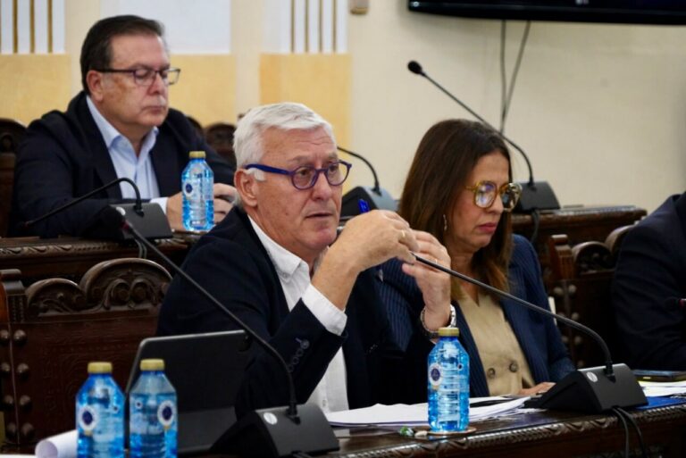 Personas sentadas en una sala institucional con micrófonos y documentos sobre las mesas.