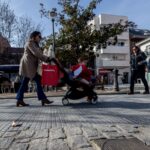 Mujer empujando un carrito de bebé en la calle con otras personas