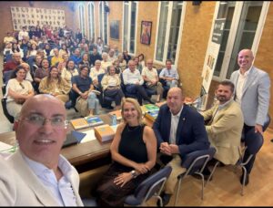 Fotografía de una sala llena de público sentado y varios libros sobre una mesa.