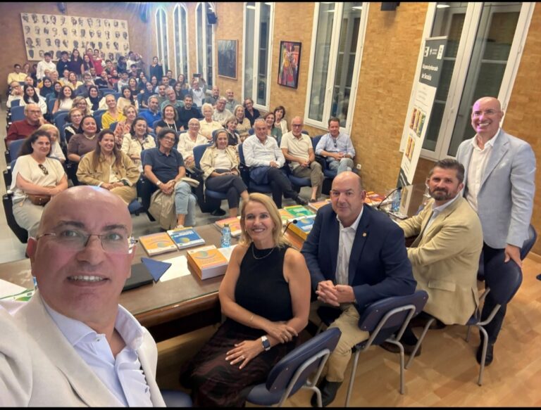 Fotografía de una sala llena de público sentado y varios libros sobre una mesa.