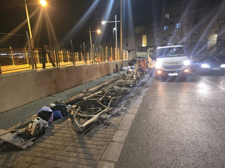 Restos carbonizados y residuos junto a una acera, con un camión detenido de noche