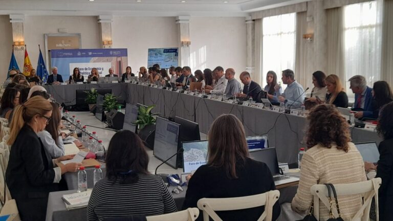 Large conference room with a long U‑shaped table of attendees, laptops, and microphones during a formal economic forum.