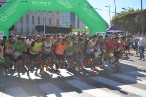 Corredores toman la salida bajo un arco verde de la Asociación Española Contra el Cáncer.