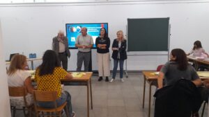 Personas reunidas en un aula mientras cuatro adultos permanecen de pie frente a una pantalla.