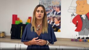 Mujer de pie en un espacio interior, con un mural ilustrado al fondo.