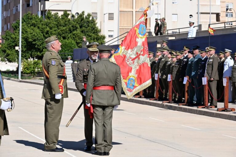 Militares uniformados participan en una ceremonia junto a un estandarte rojo en una explanada.