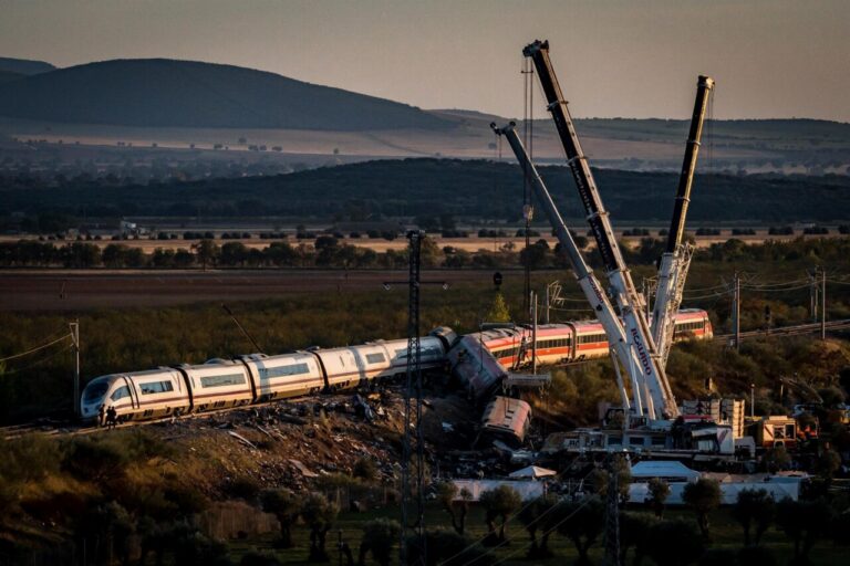 Dos trenes dañados junto a las vías, con grúas alrededor en un paisaje rural