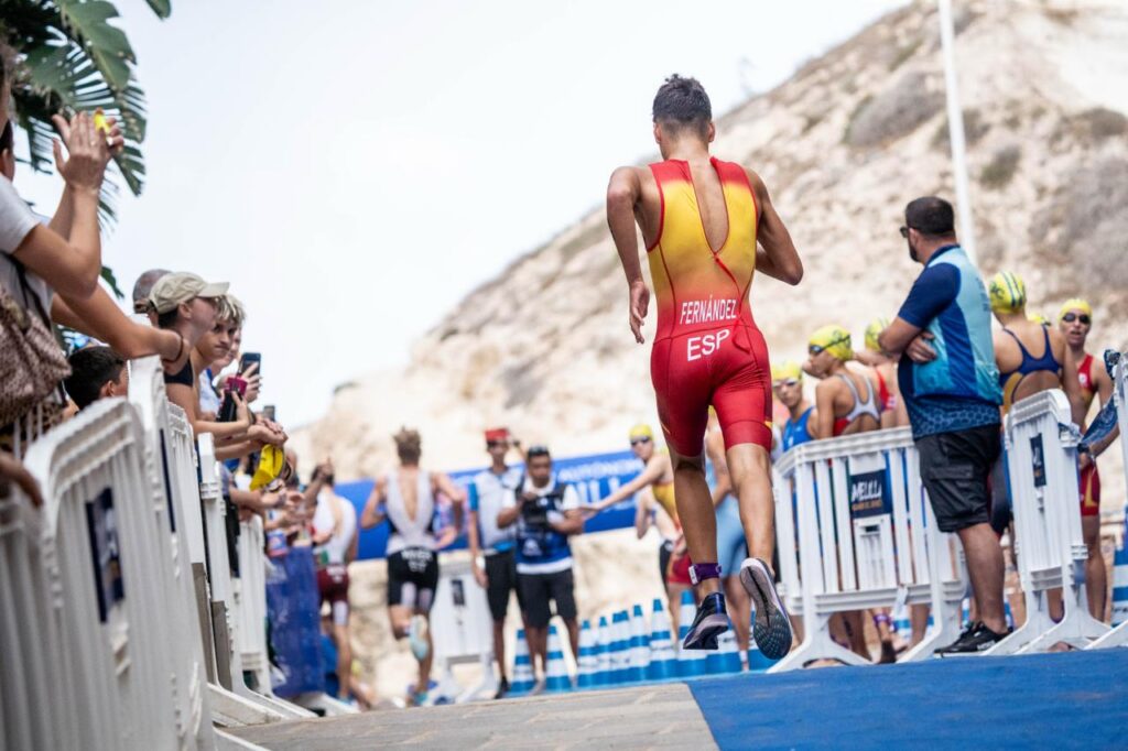 Triatleta con uniforme rojo de España corre por un pasillo delimitado por vallas.