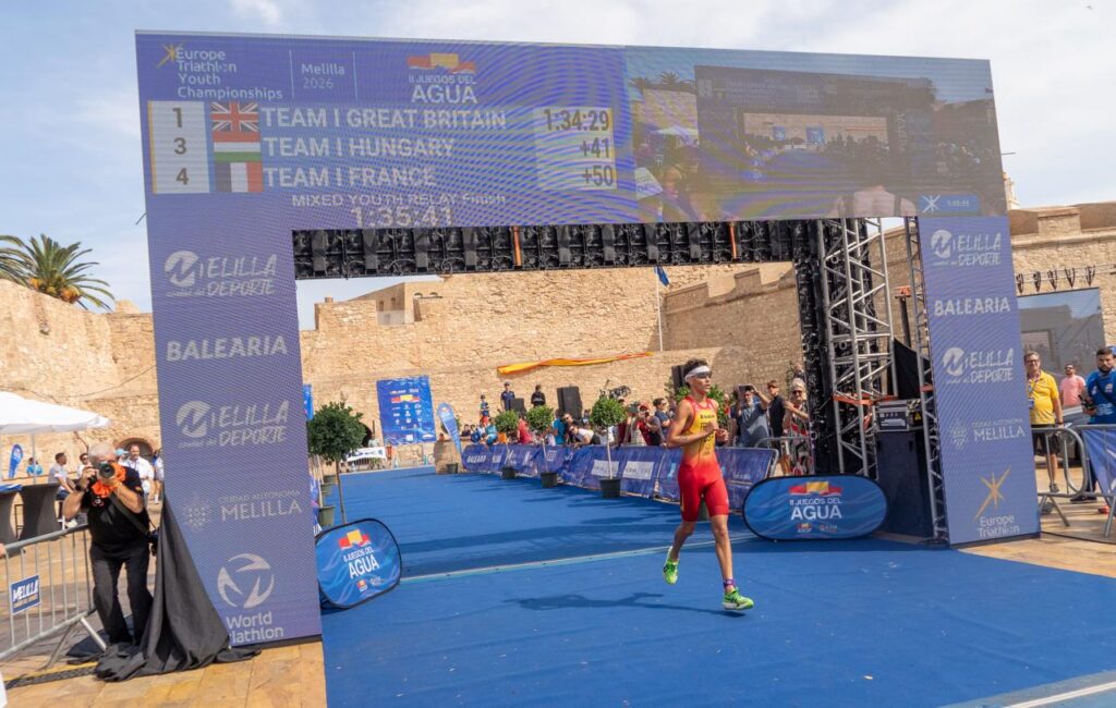 Un triatleta corre por la alfombra azul bajo el marcador del campeonato en Melilla.