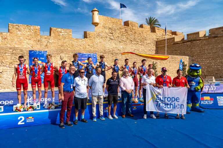 Triatletas con medallas posan junto a una plataforma y una pancarta de Europe Triathlon.