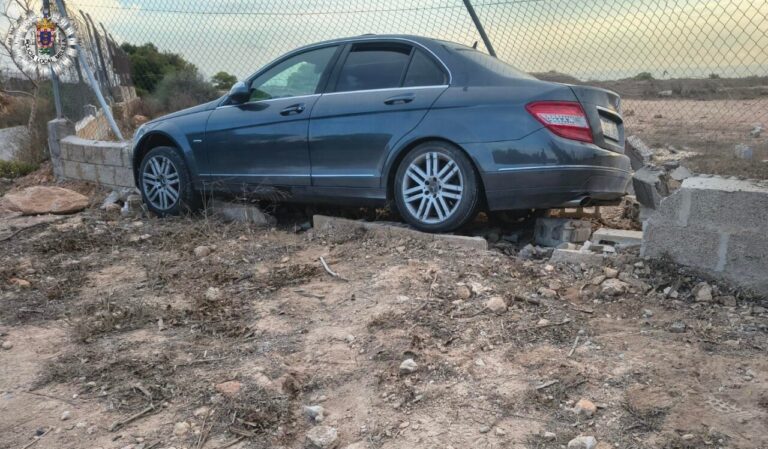 Turismo gris sobre escombros junto a un cerramiento de hormigón y malla metálica.