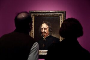 Dos visitantes observan un retrato enmarcado expuesto sobre una pared morada.