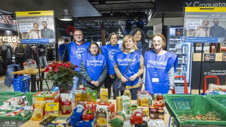 Voluntarios con chalecos azules junto a alimentos en una mesa de supermercado.