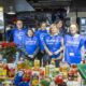 Voluntarios con chalecos azules junto a alimentos en una mesa de supermercado.